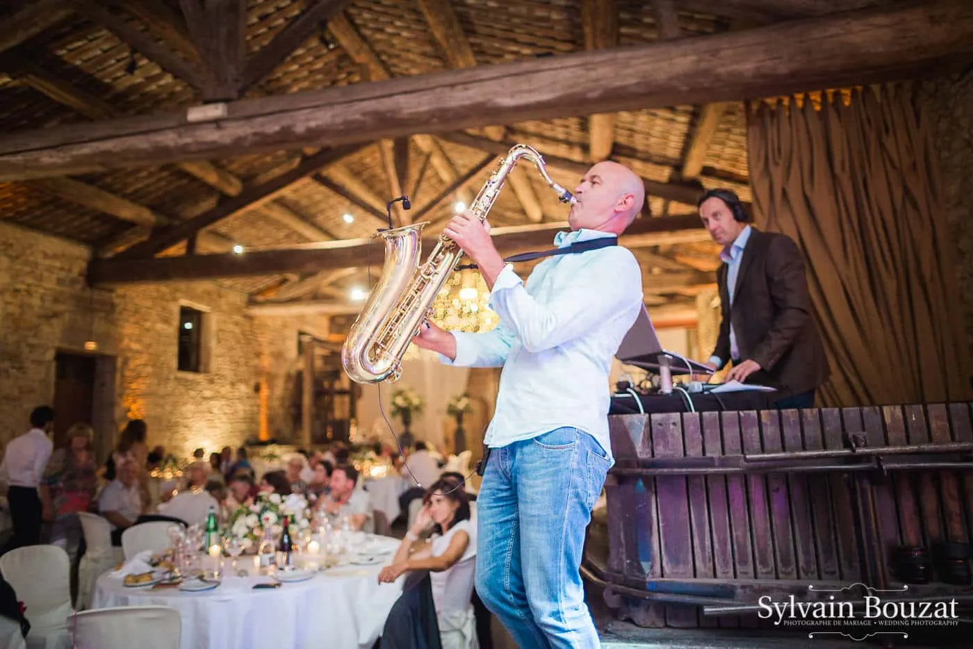 Un saxophoniste joue devant les tables, le DJ derrière sa cabine sous la charpente