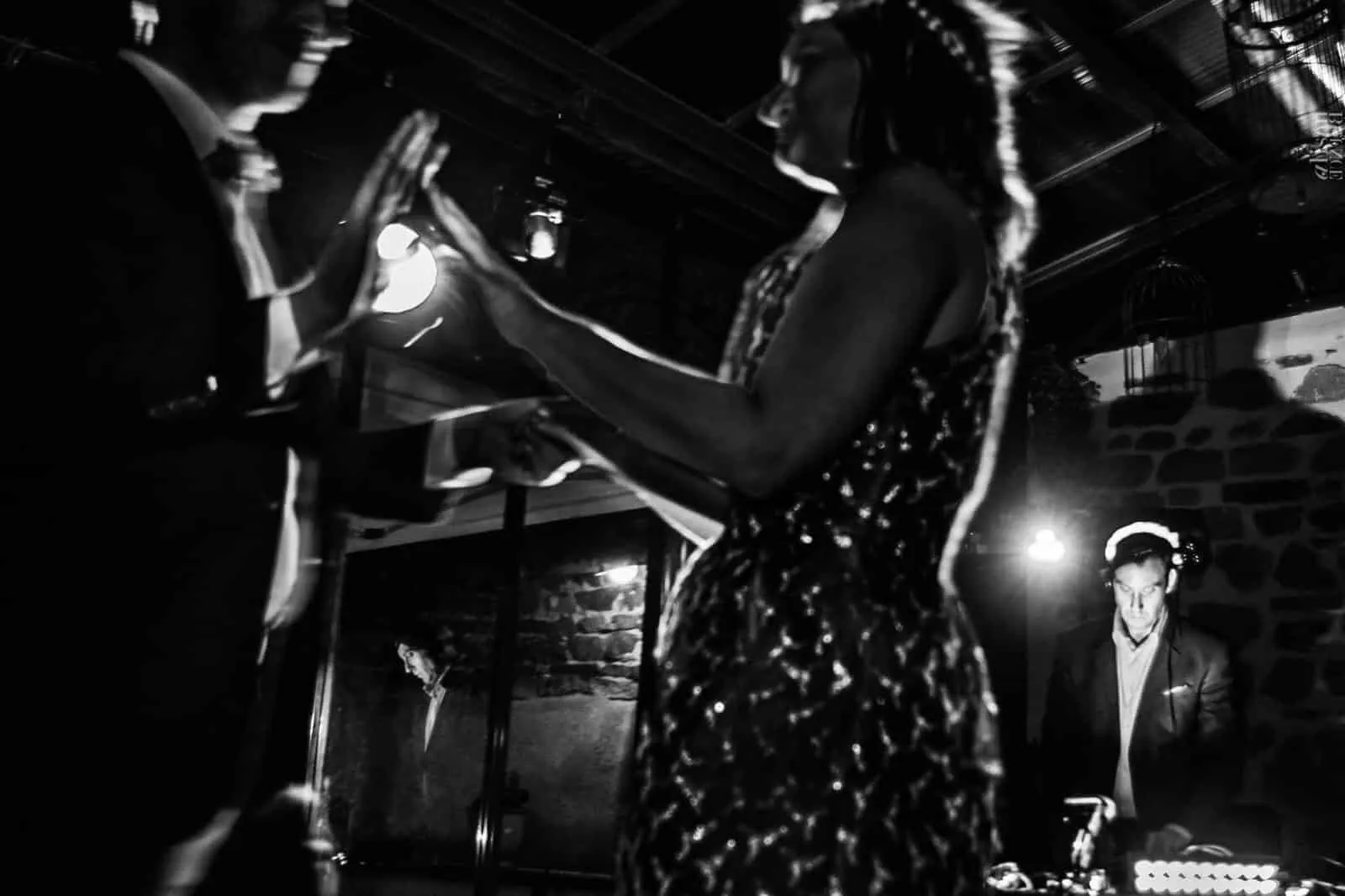 Une invitée en robe à paillettes danse, bras levé, en noir et blanc