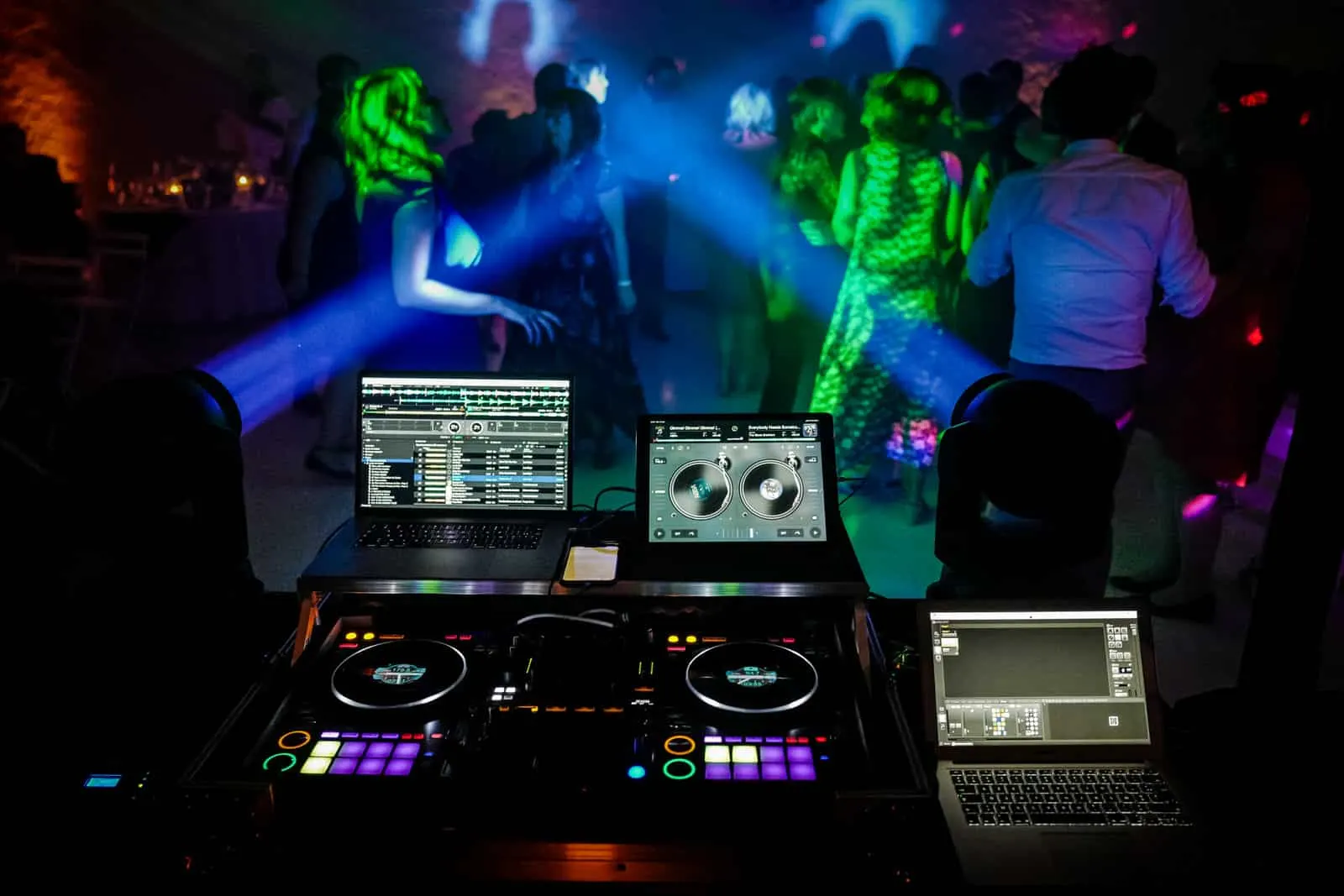 Piste de danse bondée sous les faisceaux verts et bleus, la régie du DJ au premier plan
