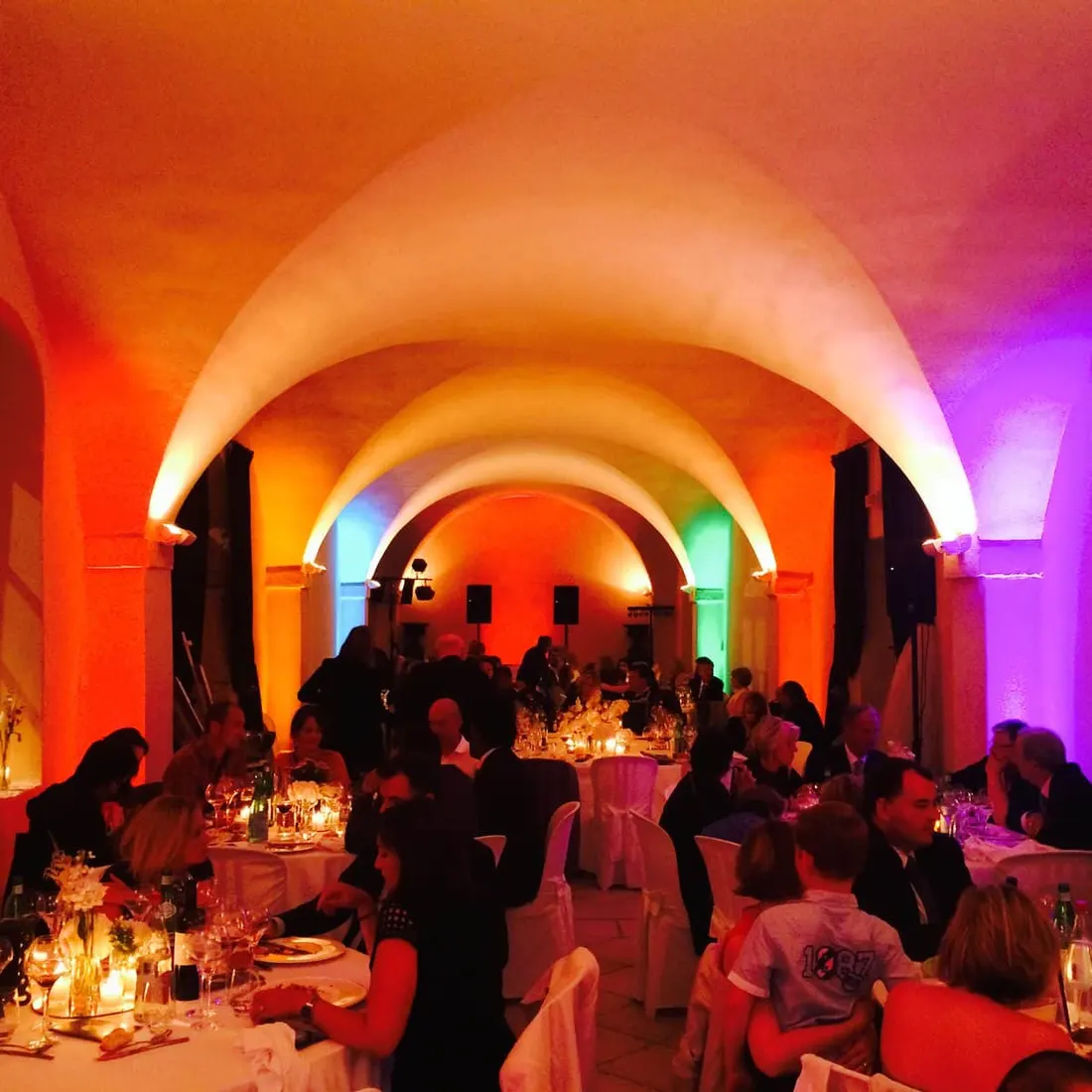Salle voûtée en pierre éclairée en orange et violet par les projecteurs LED, invités attablés